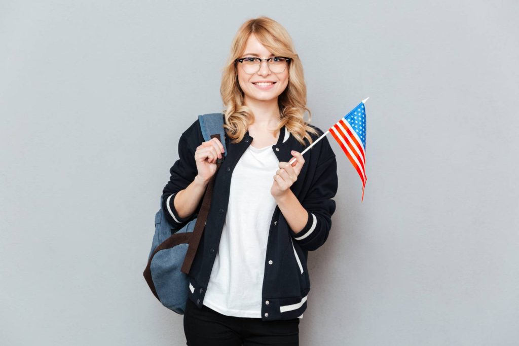 pessoa com uma mochila nas costas e segurando nas mãos uma pequena bandeira dos Estados Unidos