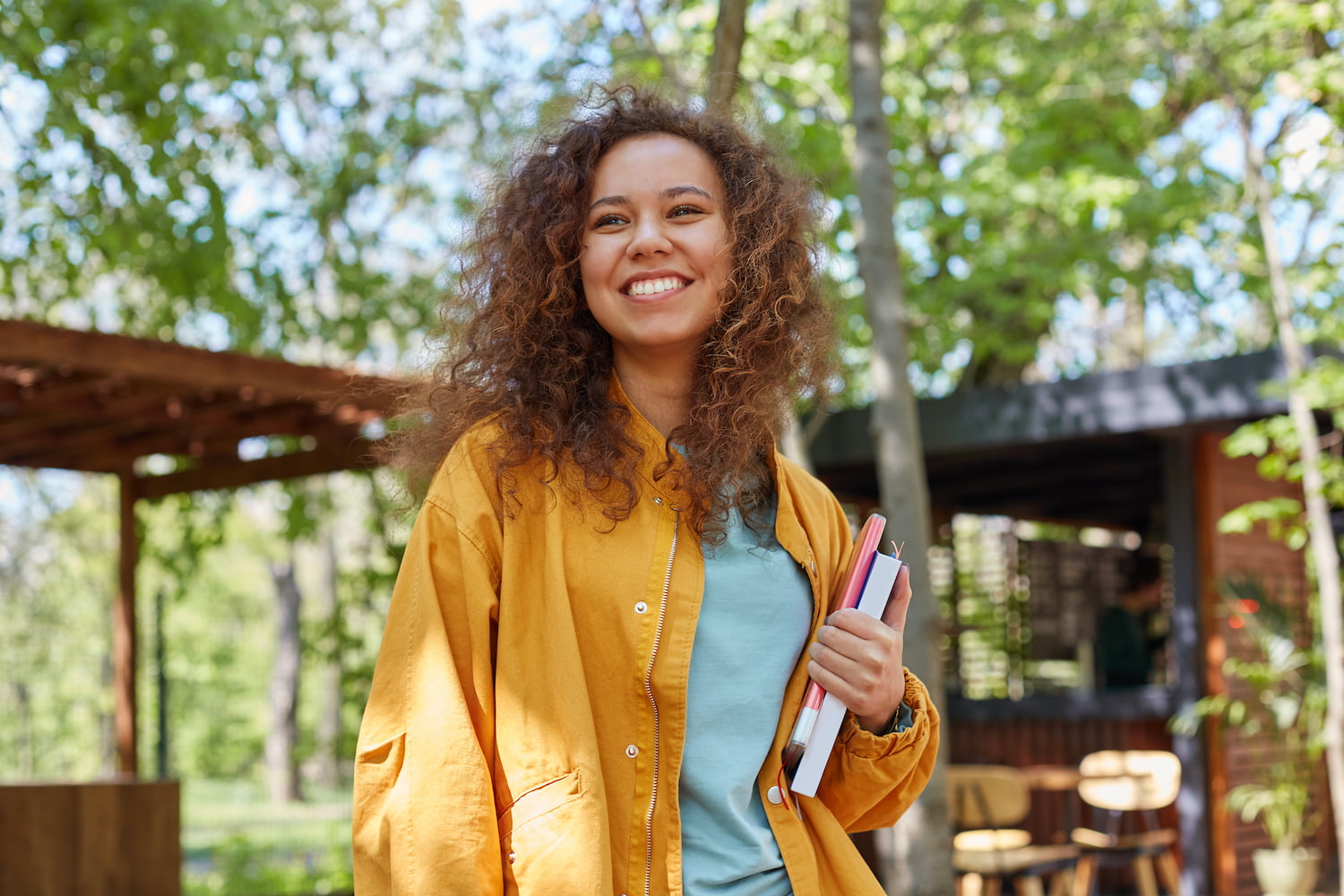 Mulher sorrindo e carregando livros no braço depois de conseguir o visto australiano de estudante.