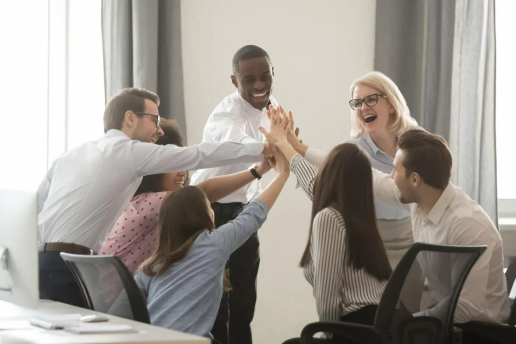 grupo de sete pessoas comemorando seus resultados dentro de uma pequena sala de escritório