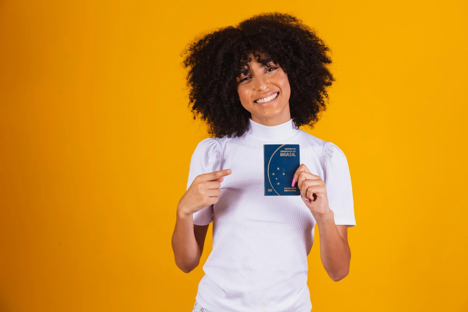Imagem de fundo amarelo com mulher negra sorrindo e segurando um passaporte brasileiro após saber como tirar passaporte.