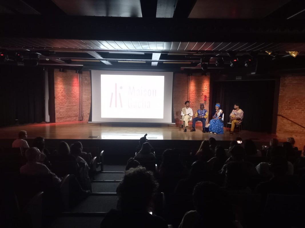foto do local do evento e três pessoas falando sob o palco do teatro