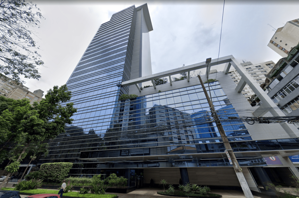 Fachada moderna e espelhada do edifício onde está localizada a unidade da One Translations em Belo Horizonte, com arranha-céus ao fundo e vegetação urbana em primeiro plano.